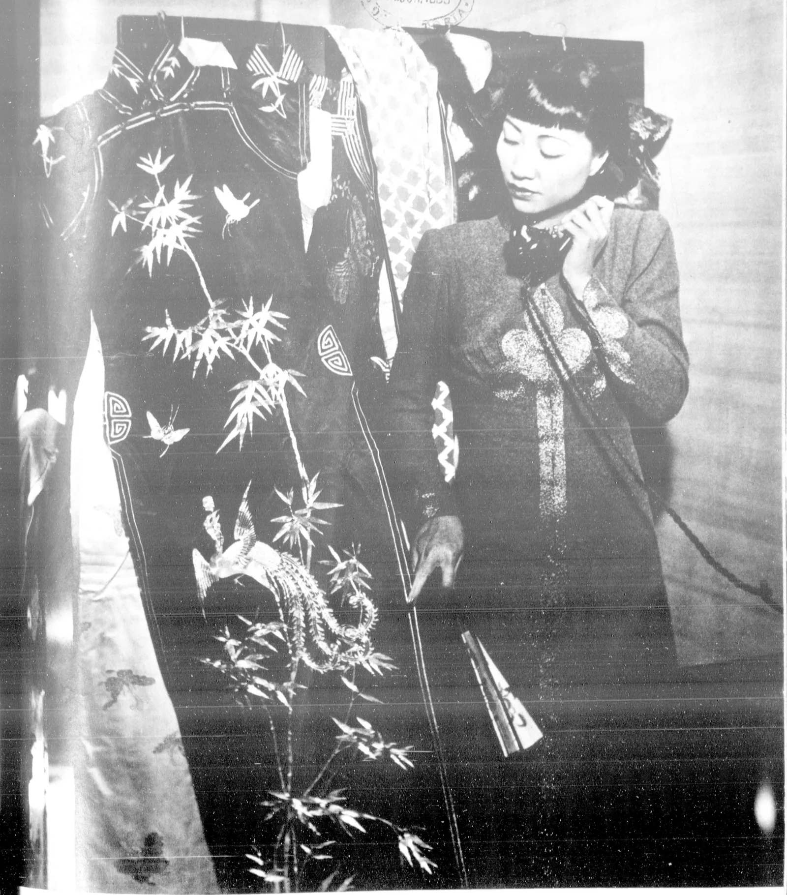 Anna May Wong on the telephone beside an open wardrobe hung with embroidered Chinese robes.